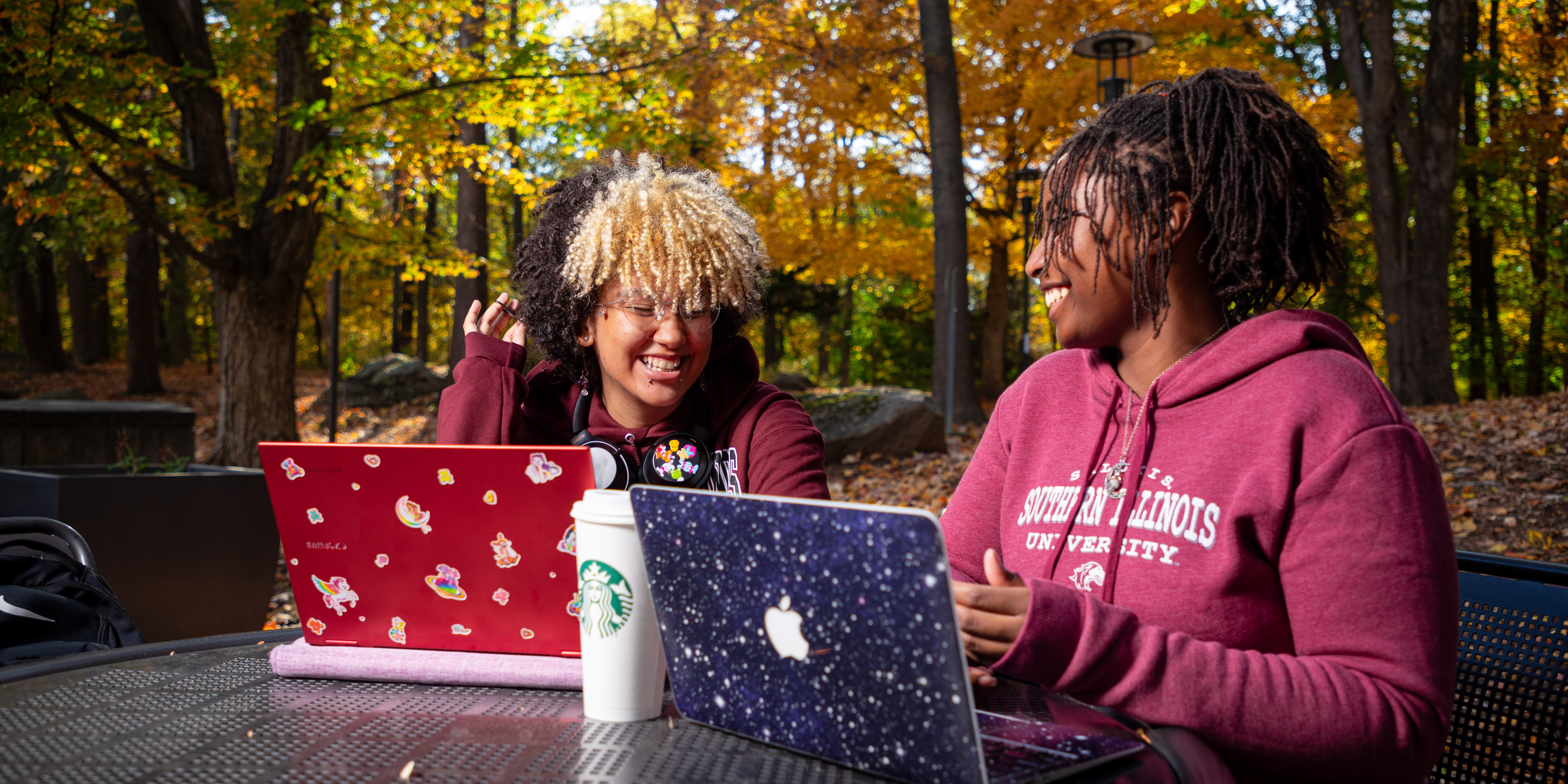 Two students studying at their computers outdoors in the fall.