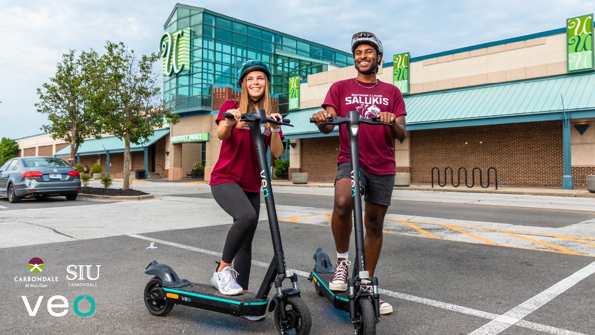 two students standing with Veo scooters